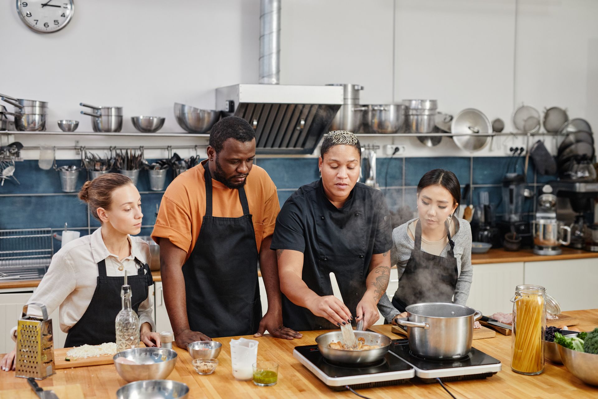 Female chef frying meat during cooking class with group of people in kitchen