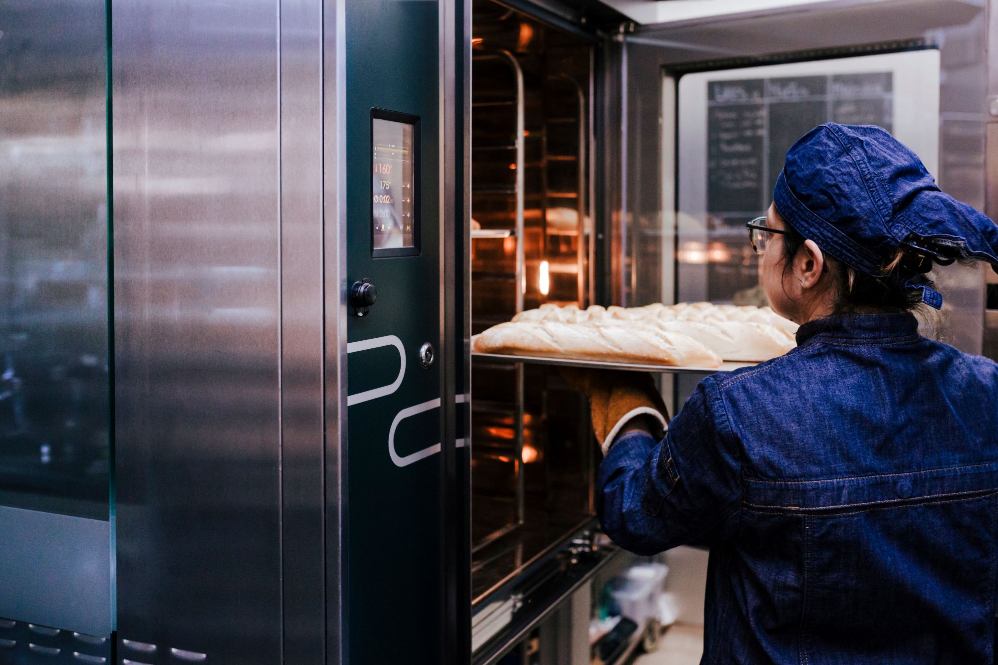 close up view of woman holding holding rack of rolls in a bakery.