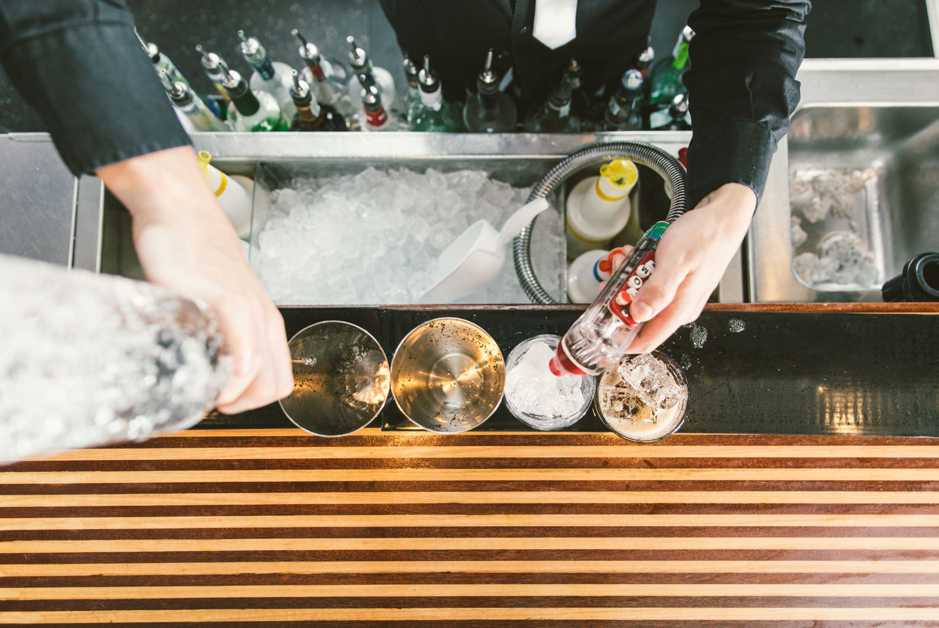 Barman at work holding soda gun in left hand and liquor bottle in right hand